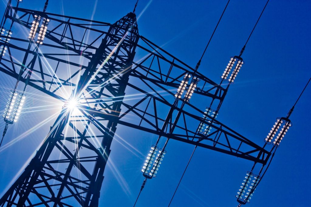 Ein Hochspannungsmasten für Strom vor blauem Himmel und Sonnenstrahlen