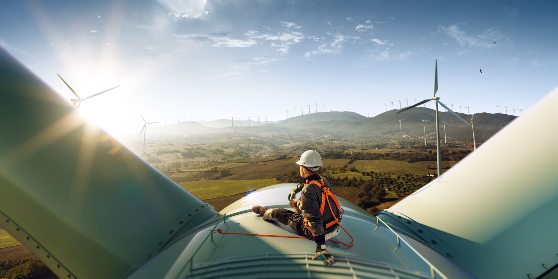 Happy engineer feel success after good work. He standing a top of windmill and looking beautiful sunset landscape